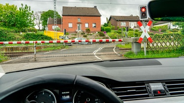 Ein Auto steht an einer Bahnschranke, die Ampel ist rot | Bild: mauritius images / Jochen Tack / Alamy / Alamy Stock Photos